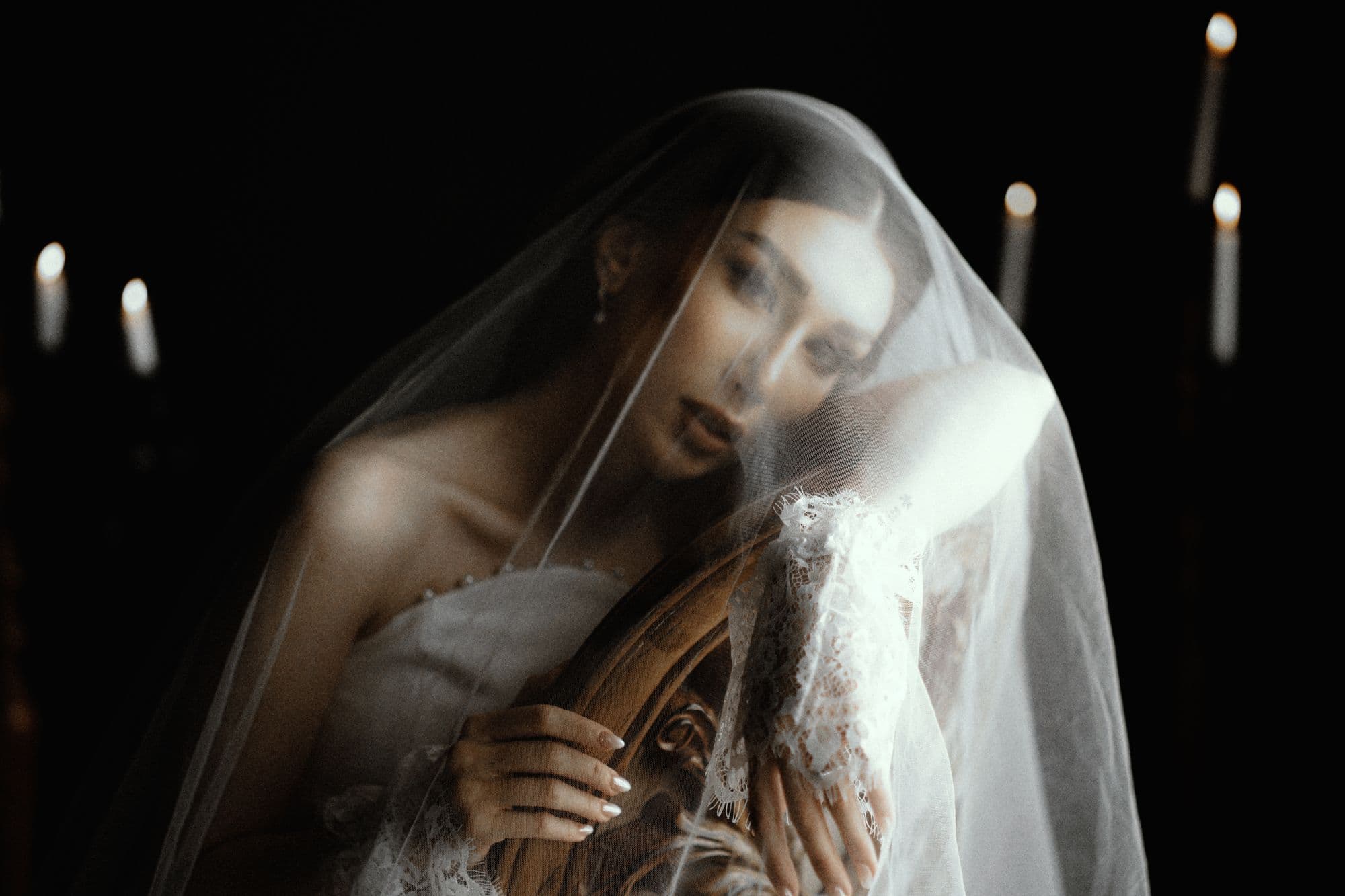 Bride in a lace veil lit by candlelight in a darkened room