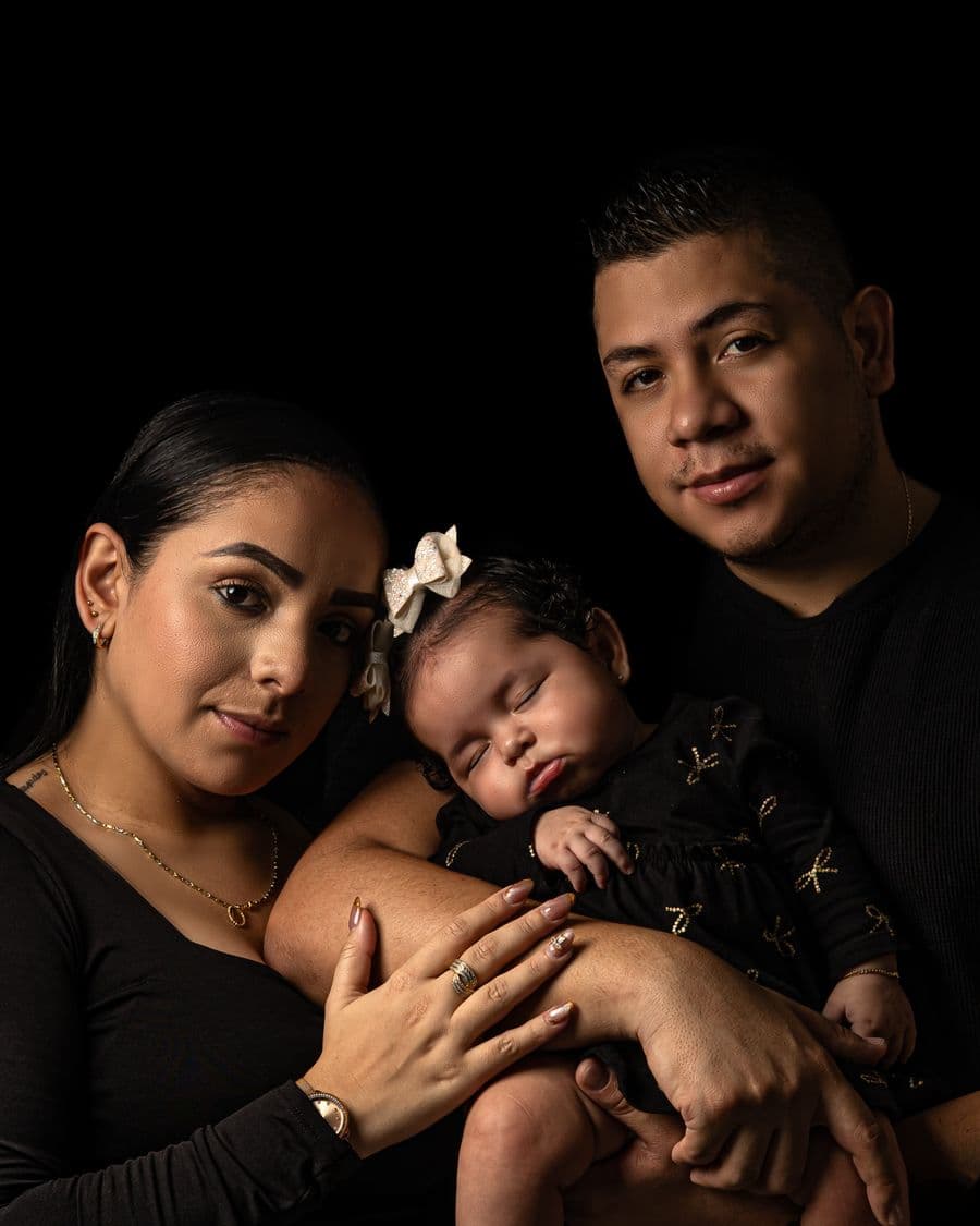 Parents holding their sleeping newborn against a black background