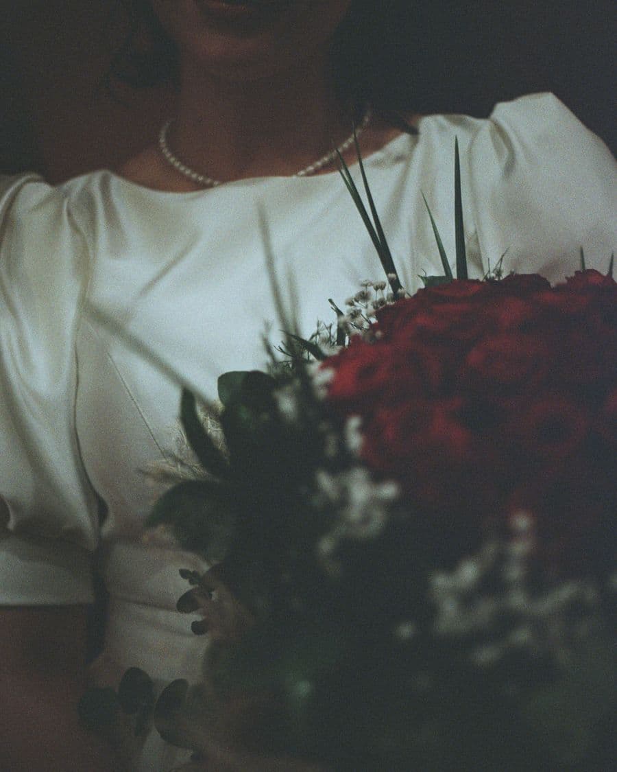 Bride holding a bouquet of red roses in low light