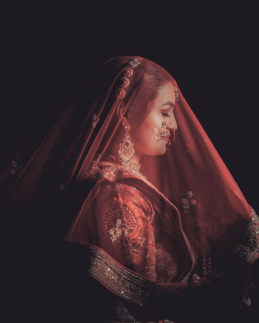 Bride in embroidered traditional attire lit against a dark backdrop